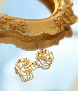Gros plan de boucles d'oreilles à pompons dorées à plusieurs niveaux sur un miroir