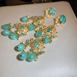 Détail de boucles d'oreilles vintage dorées avec motifs de fleurs et perles en résine bleues