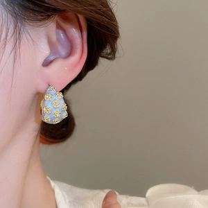 Detail of light blue enamel C-shape hoop earring with gold flower inlay and crystals