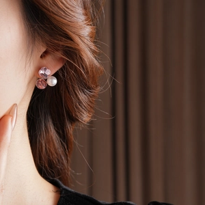 Close-up of pink crystal and white pearl cluster stud earrings worn by a model