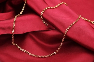 Detail of a polished gold O-link chain necklace displayed on dark red silk background