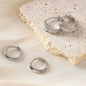 Detail of silver pleated hoop earrings with zircon accents on a textured stone surface