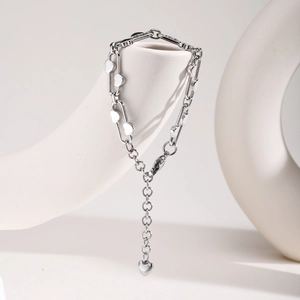 Detail of stainless steel paperclip chain bracelet with heart charms on white stone
