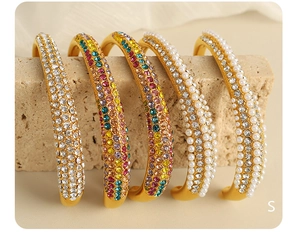 Detail of gold open bracelets featuring pearls and colorful rhinestones on stone