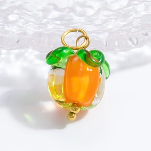 Handmade glass persimmon pendant with green leaves and gold ring on water-textured surface