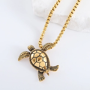 Detailed close-up of a golden turtle pendant with box chain on a white marble stone