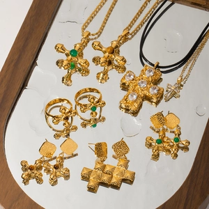 Close-up of 18K gold plated cross necklaces and rings with emerald green gemstones