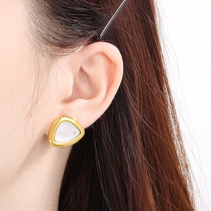Gros plan sur un clou d'oreille triangle doré avec nacre blanche et pierre de zircon