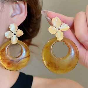 Detailed view of large amber resin ring earrings with gold floral stud and brushed texture