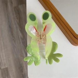 Draufsicht auf eine grüne Frosch-Haarklammer aus Acetat mit goldener Metallfeder