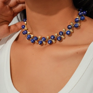 Close-up of royal blue bead necklace with golden leaf accents on a model's collarbone