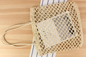 Detail of beige hand-woven hollow tote bag with textured mesh structure on wood table