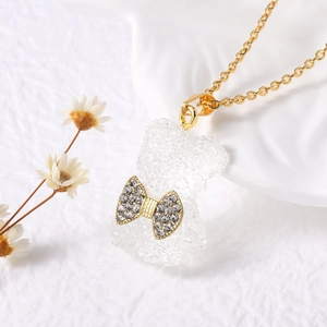 Dettaglio di una collana placcata oro con ciondolo a forma di orso bianco traslucido e fiocco