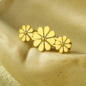 Close-up of golden metal hair clip featuring three daisies on a textured sandy surface