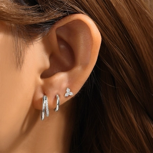Close-up of three-piece silver earring set with studs and hoops worn on ear