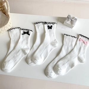 Detailed flat lay of white Lolita style socks with black and pink bows and ruffled edges