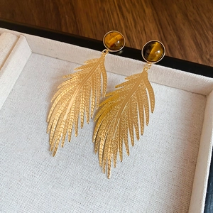 Detailed close-up of golden leaf earrings with brown tiger eye beads on beige fabric