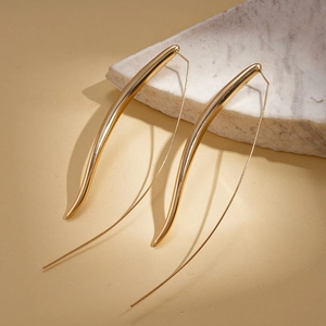 Detailed view of long gold teardrop hook earrings on marble texture background