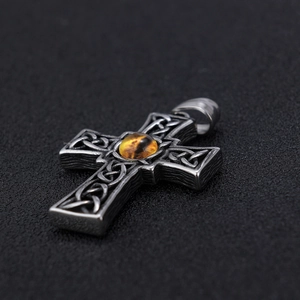 Macro view of vintage silver Celtic cross pendant with an amber gemstone and wood texture