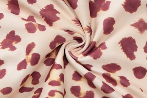 Close-up of leopard print fabric texture in beige with burgundy and yellow spots