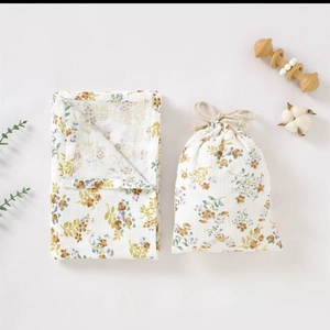 Floral muslin baby blanket and matching drawstring bag on neutral background