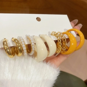 Détail de cinq paires de créoles minimalistes en acrylique et or avec des perles