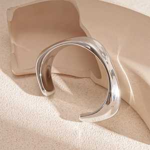 Close-up of a silver wavy irregular open bangle with a polished mirror finish on a pedestal