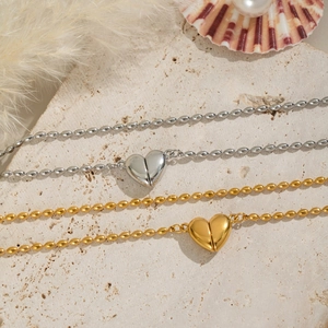 Détail de colliers perlés en or 18 carats et argent avec pendentifs cœur sur pierre texturée