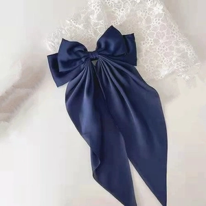 Detail of navy blue satin bow hair clip with long streamers on white lace backdrop