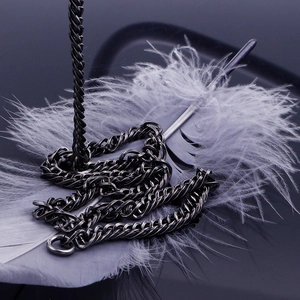 Detail of dark gray titanium steel Cuban link chain draped over a soft gray feather