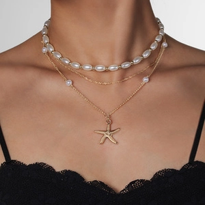 Close-up of layered gold necklace with white pearls and a detailed starfish pendant