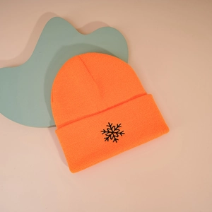 Détail du bonnet en tricot orange vif avec broderie de flocon de neige noir sur le revers