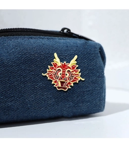 Macro detail of cartoon dragon enamel pin styled on dark blue denim fabric accessory