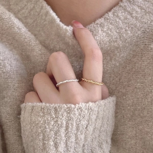 Detail of twisted knot woven rings in gold and silver finish on a model's finger