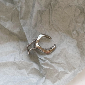 Detailed view of silver C-shaped ear cuff with beaded chain on crinkled paper background