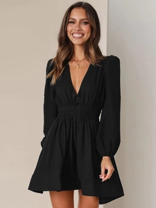 Dettaglio di un abito nero con scollo a V profondo, maniche lunghe e vita plissettata elegante
