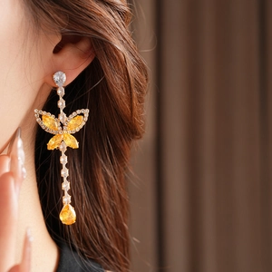 Detail of gold butterfly earrings with yellow teardrop pendant on model's ear
