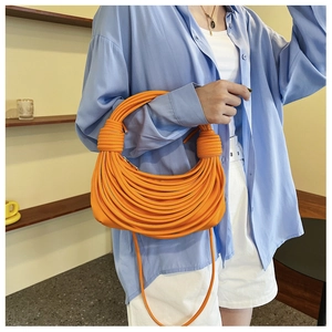Dettaglio della borsa a mano arancione intrecciata con nodi decorativi e tracolla fine
