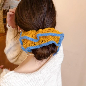 Close-up of yellow knitted flower scrunchie with blue wavy edges on a ponytail