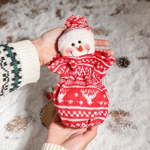 Festive knitted snowman Christmas gift bag with drawstring held in hand on snowy background