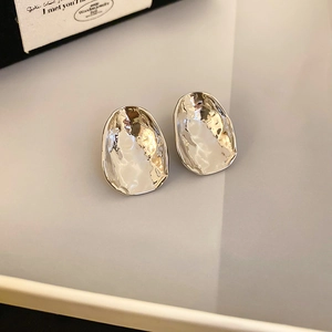 Detailed macro view of irregular silver stud earrings with organic hammered metal texture