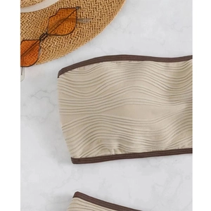 Dettaglio del top bikini a fascia beige con trama ondulata e bordo marrone scuro
