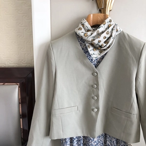 Detail of light green collarless jacket with fabric buttons and white floral silk scarf
