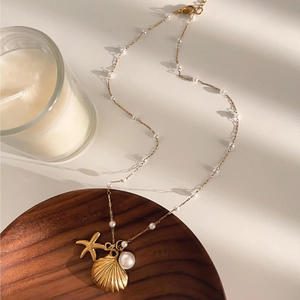 Marine themed gold necklace with starfish, seashell pendants and pearls on a wooden tray
