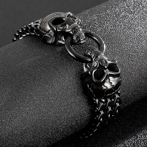 Detailed view of matte black skull charm and thick punk style metal link chain bracelet