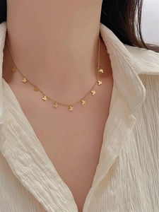Detail shot of a delicate gold butterfly necklace on a model's neck with silk shirt