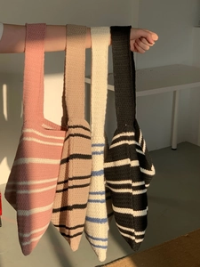Detail showing hand holding four striped knitted tote bags in pink, khaki, white and black
