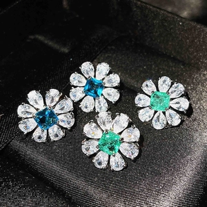 Macro shot of flower-shaped earrings with sky blue and emerald gemstones on black silk