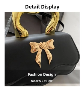 Detail of elegant black leather handbag with a gold heart bow and unique metal handle
