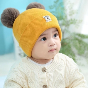Close-up of yellow baby knit beanie with two brown pom-poms and warm cable knit texture